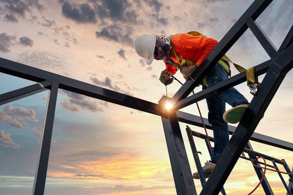 Industrial worker welding at height using safety harness and protective gear